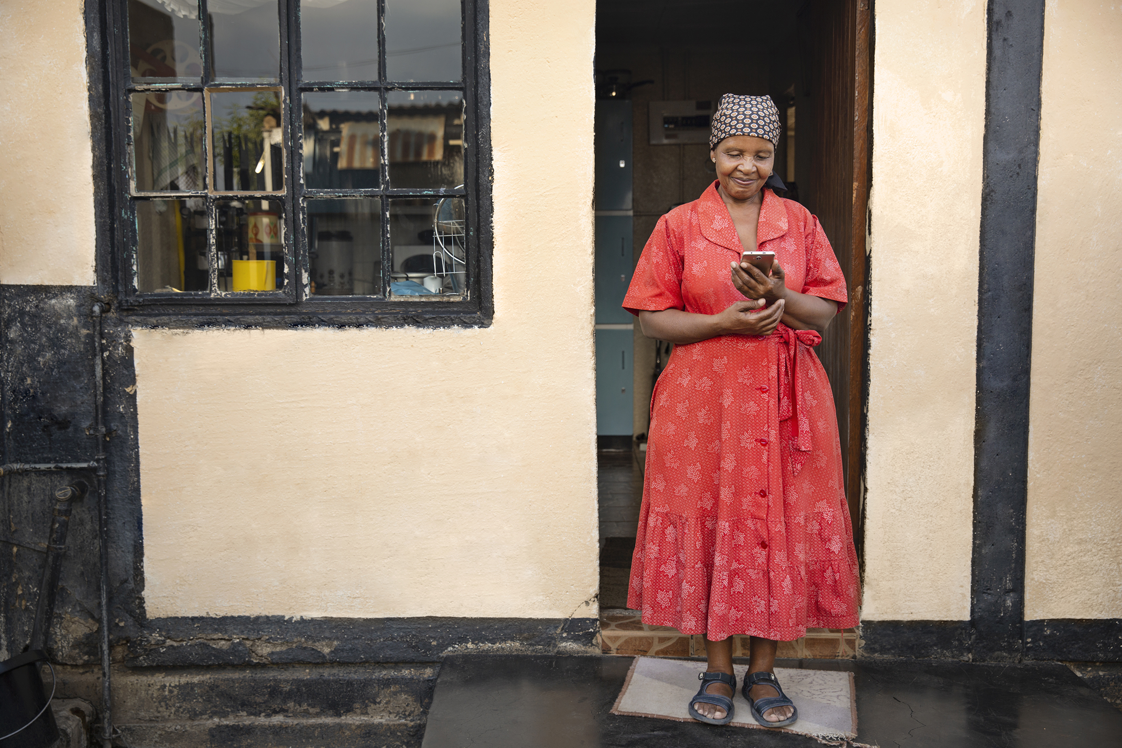 Older South African lady on her phone while standing outside her kitchen door