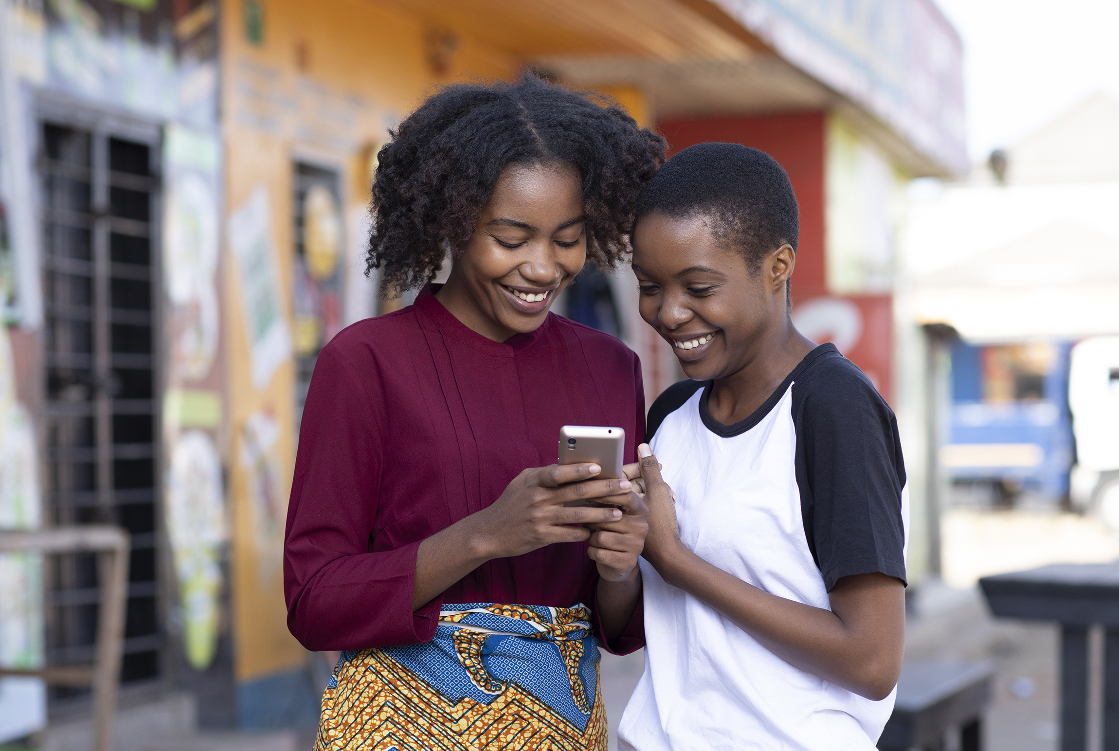 Two young Zambian friends laughing in the street while looking at a mobile phone