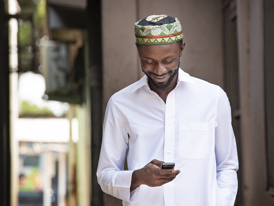 Muslim man walking down the road in Ghana, looking at Facebook on his mobile